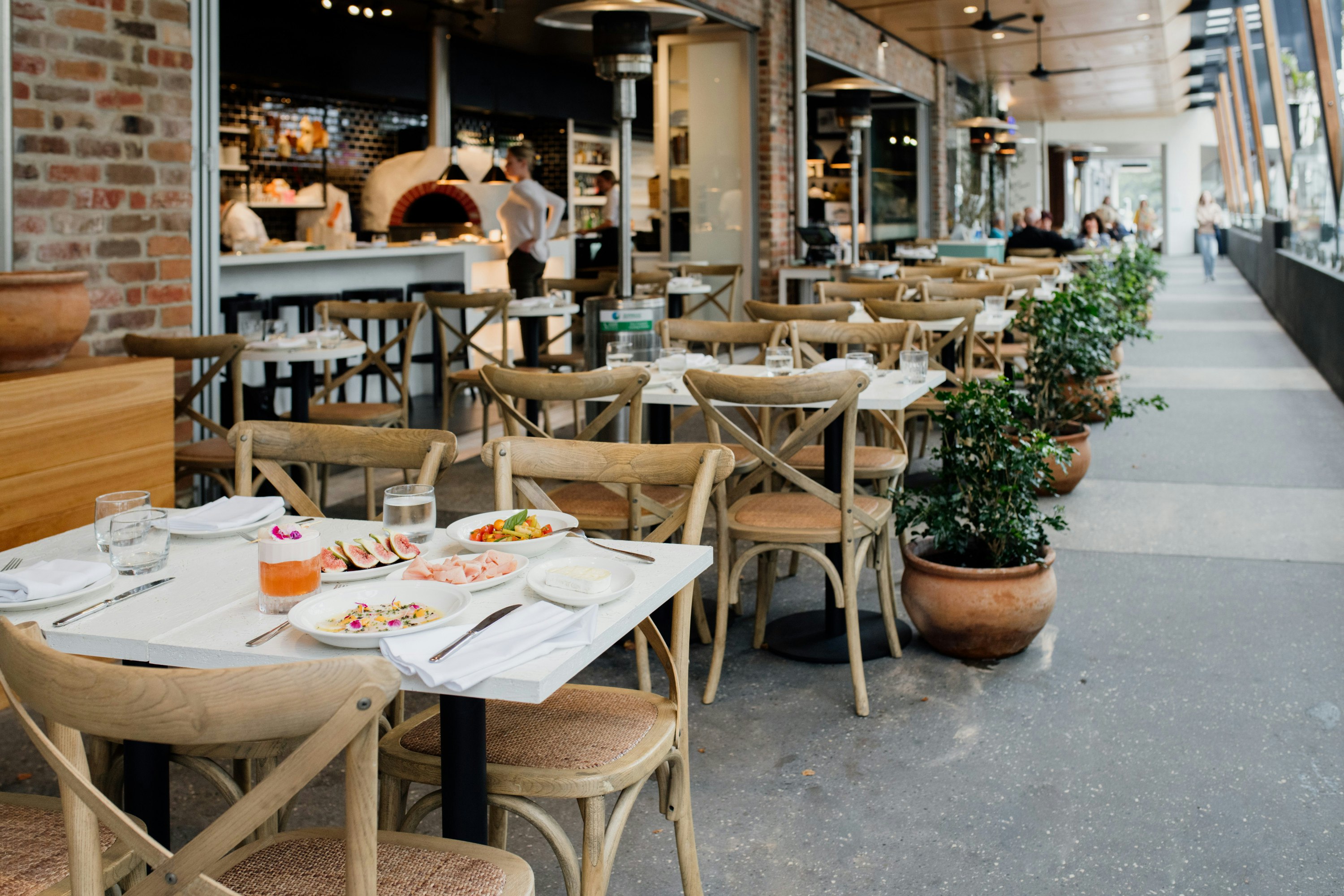 the exterior of a restaurant with rattan chairs and potted plants
